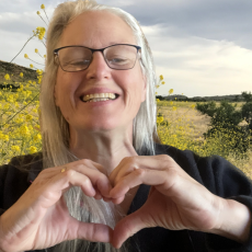 安娜·卡尔森教授在一片野花前微笑着用手做了一个心形. 